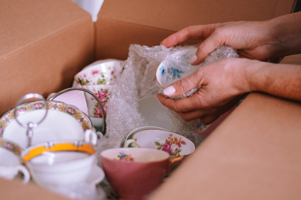 Woman is packing fine china dishes into cardboard box for moving