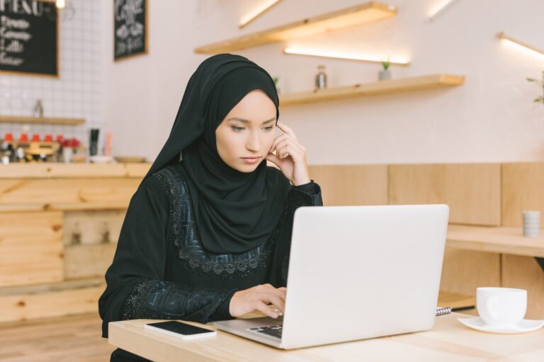 concentrated young muslim woman using laptop in cafe